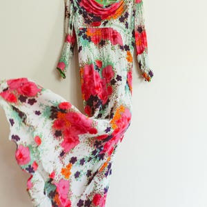 May include: A white maxi dress with a floral print in shades of pink, orange, green, and purple. The dress has a cowl neck and long sleeves.