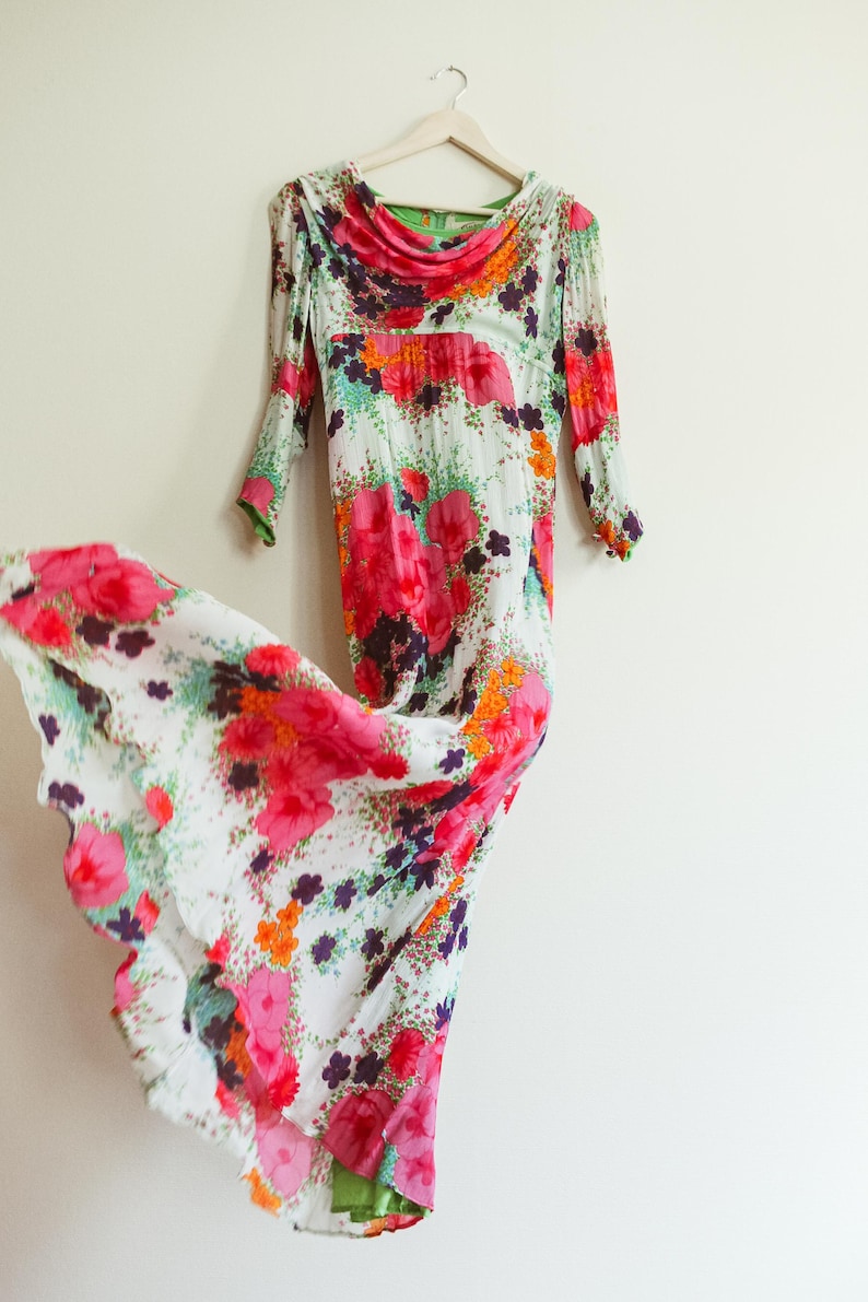 May include: A white maxi dress with a floral print in shades of pink, orange, green, and purple. The dress has a cowl neck and long sleeves.