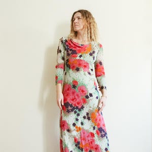 May include: A long, flowing maxi dress with a floral print in shades of pink, orange, green, and purple. The dress has a cowl neck and three-quarter sleeves.