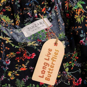 May include: Black floral print top with a tag that reads "Long Live Butterflies." The top has a round neckline and a button closure. The tag also has the text "ZINZANE RIO DE JANEIRO."