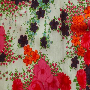 May include: A white fabric with a floral pattern. The pattern features pink, red, orange, and blue flowers on a white background.