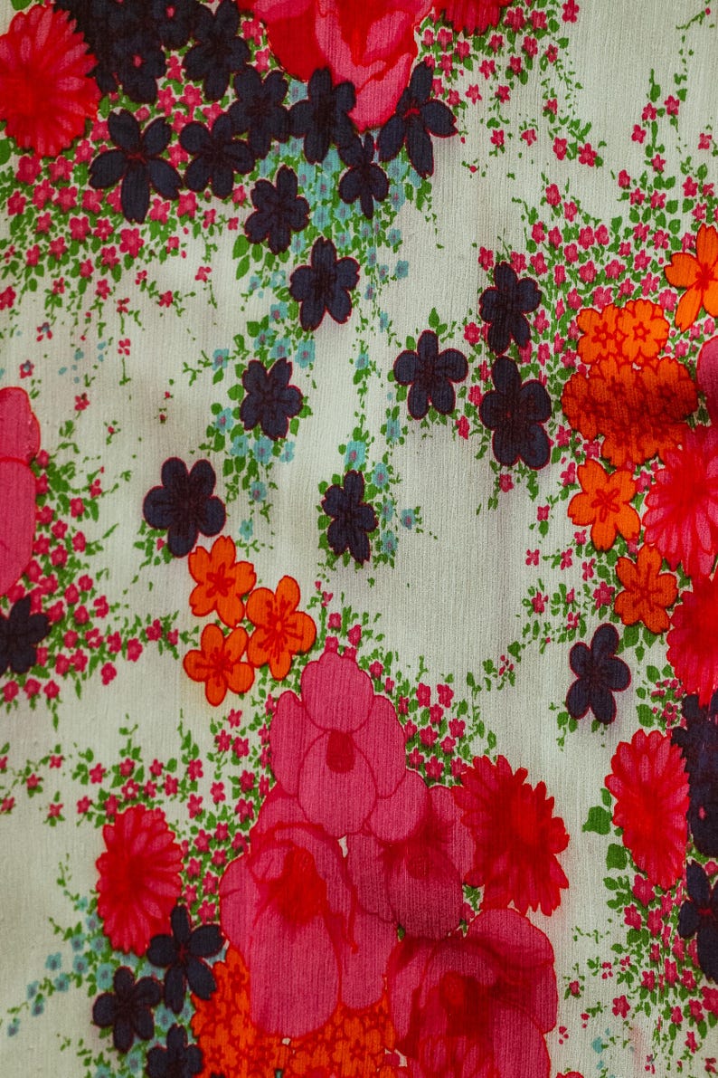 May include: A white fabric with a floral pattern. The pattern features pink, red, orange, and blue flowers on a white background.
