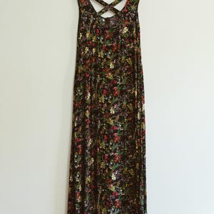 May include: A black maxi dress with a floral pattern in red, yellow, and green. The dress has a crisscross back design and hangs on a wooden hanger against a white wall.