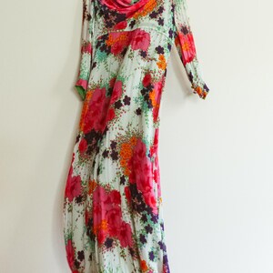 May include: A long, flowing white dress with a floral print in shades of pink, orange, and green. The dress has a scoop neck and three-quarter sleeves.