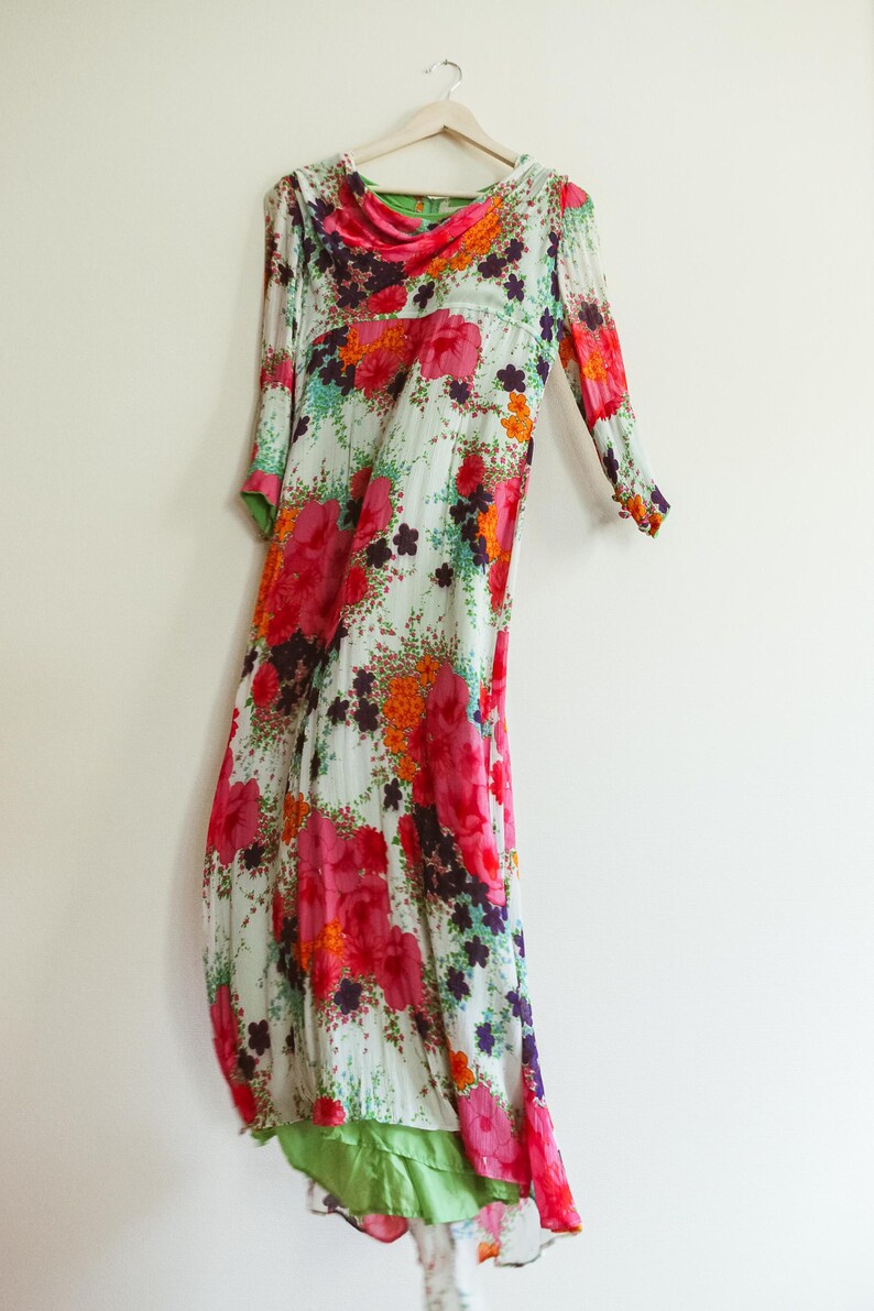 May include: A long, flowing white dress with a floral print in shades of pink, orange, and green. The dress has a scoop neck and three-quarter sleeves.