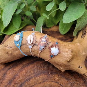 Può includere: Quattro braccialetti in macramè fatti a mano con diverse conchiglie. I braccialetti sono realizzati con cordoncino blu, marrone e beige e presentano una varietà di conchiglie.