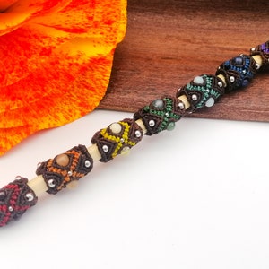 May include: Seven chakra beads strung on a wooden dowel. Each bead is a different color and has a gemstone in the center. The beads are brown, red, orange, yellow, green, blue, and purple.