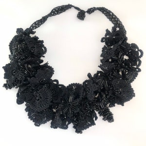May include: A black beaded necklace with a floral design. The necklace is made of small black beads that are woven together to create a delicate and intricate pattern.
