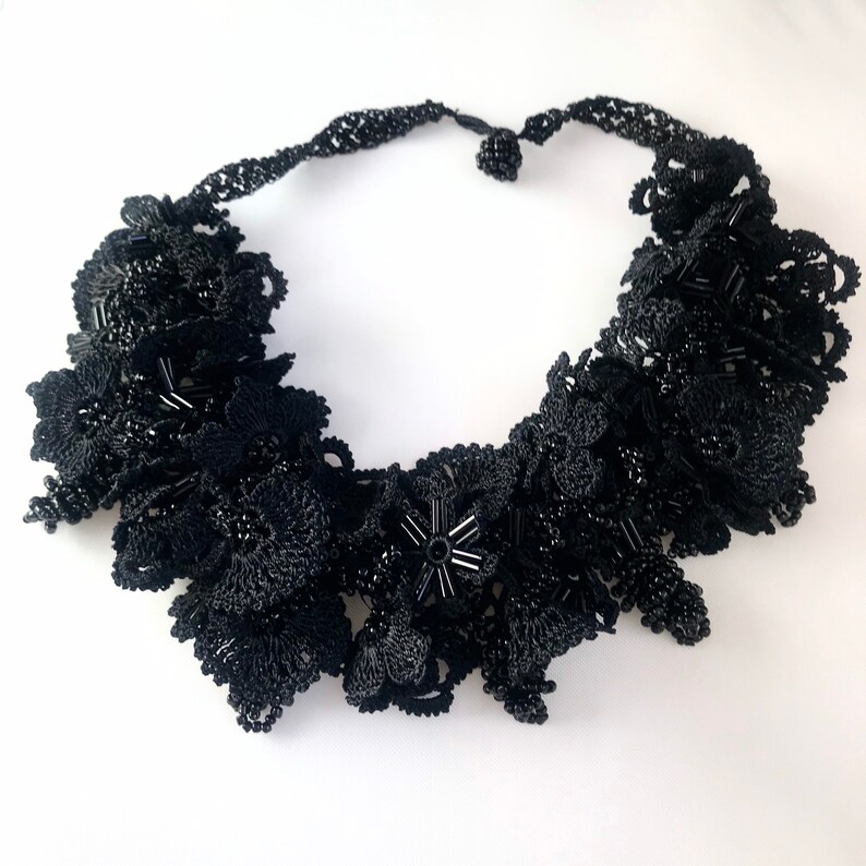 May include: A black beaded necklace with a floral design. The necklace is made of small black beads that are woven together to create a delicate and intricate pattern.