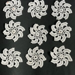 May include: Nine white crocheted doilies with a spiral design. The doilies are arranged in a grid pattern on a black background.