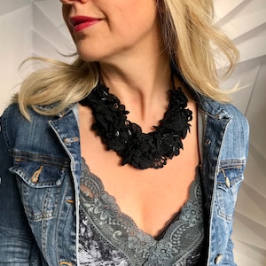 May include: A black lace choker necklace with multiple layers of ruffles. The necklace is worn by a person with blonde hair and a denim jacket.