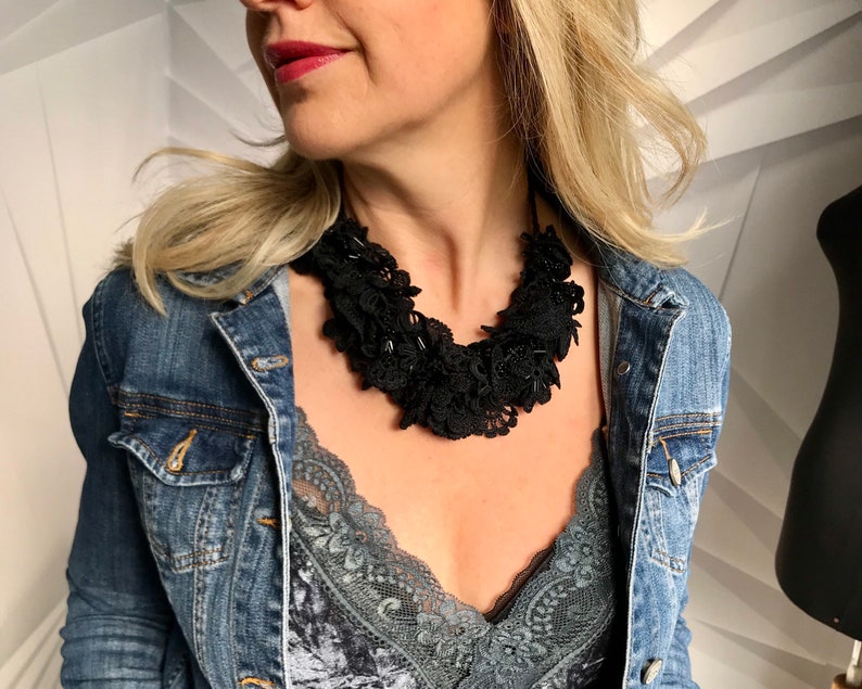 May include: A black lace choker necklace with multiple layers of ruffles. The necklace is worn by a person with blonde hair and a denim jacket.