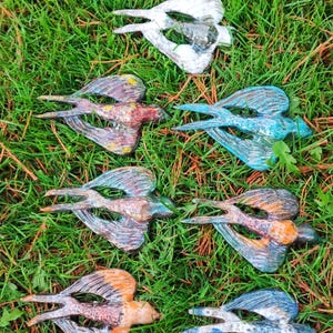 May include: Seven ceramic swallow bird sculptures in various colours, including blue, white, orange, and brown, are arranged on a bed of green grass.