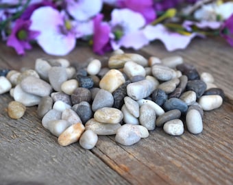 May include: A pile of smooth, gray, white, and brown river rocks on a wooden surface.