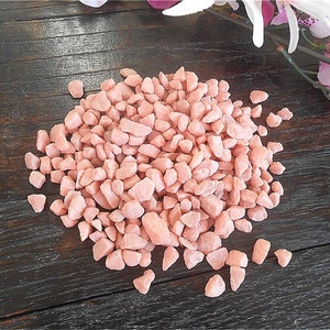 May include: A pile of small, pink, decorative gravel stones. The stones are irregularly shaped and have a slightly rough texture.