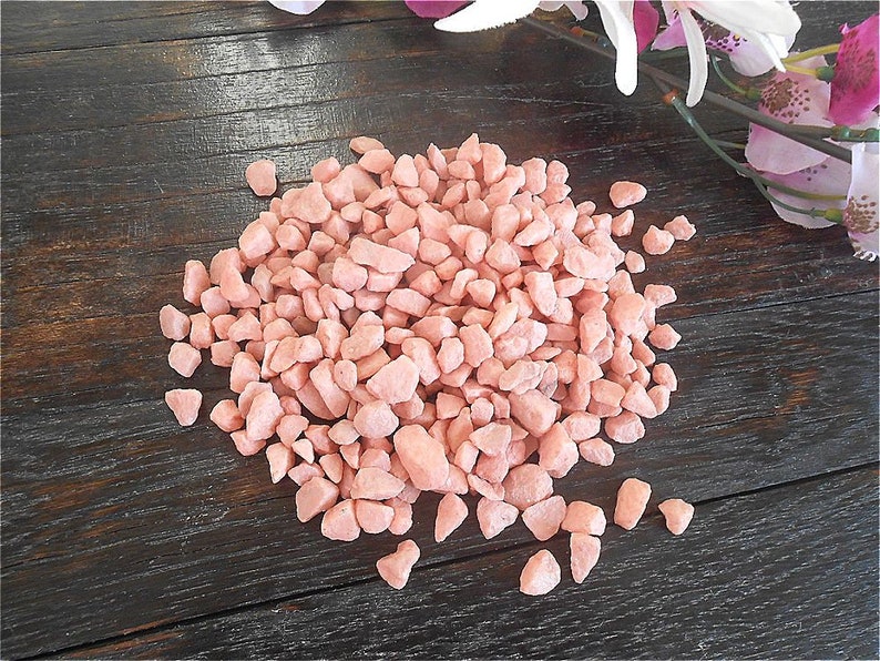 May include: A pile of small, pink, decorative gravel stones. The stones are irregularly shaped and have a slightly rough texture.