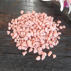 May include: A pile of small, pink, irregular shaped gravel stones on a dark brown wooden surface.
