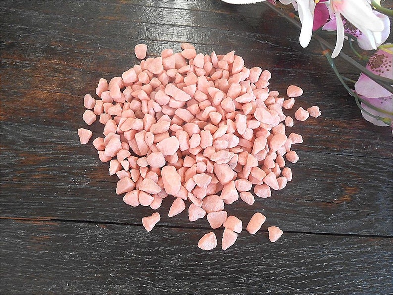 May include: A pile of small, pink, irregular shaped gravel stones on a dark brown wooden surface.