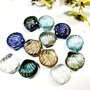 May include: Assortment of iridescent glass seashells in various colors, including blue, green, brown, and white. The shells are arranged on a white surface.
