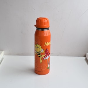 Puede incluir: Botella de agua aislada de color naranja con un personaje de abeja de dibujos animados y una seta de lunares rojos y blancos. La botella tiene una tapa naranja a juego y la palabra "Maja" está impresa en el lateral.