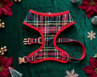 May include: A pet harness featuring a black, red, and green plaid pattern with bright red trim. The harness includes rose gold metal buckles and adjustable sliders, designed with a contoured chest piece and straps for a secure fit around the torso.