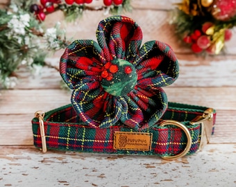 May include: A festive dog collar and flower accessory set. The collar and flower are made of red, green, and yellow plaid fabric. The flower has a green center with red berry accents. The collar has a gold-colored buckle and a small brown tag with text.