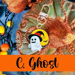 May include: A Halloween-themed keychain featuring a white ghost wearing a black hat, set against a yellow moon with a bat. The keychain has a silver clasp. The text "C. Ghost" is displayed on an orange banner.