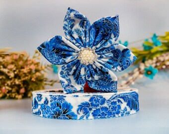 Op de afbeelding: Een blauwe en witte bloem van stof met een bloemenprint en een parel in het midden, liggend op een blauw en wit lint van stof met een bloemenprint.
