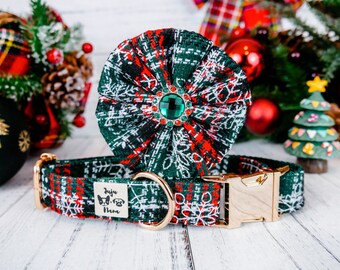 May include: A Christmas-themed dog collar and matching flower accessory. The collar and flower are green, red, and white with a snowflake pattern. The collar has a gold-colored buckle and a small tag with a logo. The flower has a large green jewel in the center.