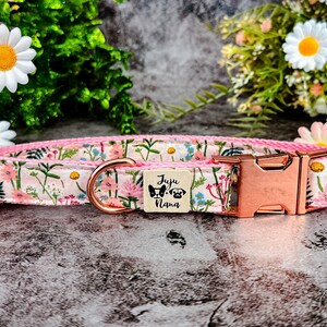 Puede incluir: Collar para perros con estampado floral sobre fondo rosa, adornado con flores rosas, azules y verdes. Hebilla de oro rosa y peque&ntilde;a etiqueta de madera con la inscripci&oacute;n "Juju Nana" e ilustraciones de perros.