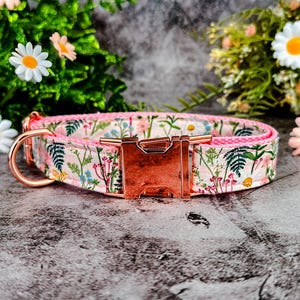 Puede incluir: Un collar floral para perros con fondo rosa y hebilla de oro rosa. El collar presenta un estampado de flores silvestres y vegetaci&oacute;n. La ferreter&iacute;a incluye una anilla en D y un cierre met&aacute;lico.