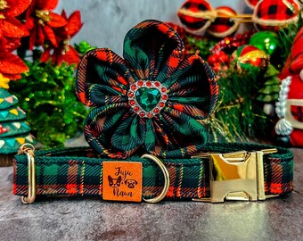 May include: A green, red, and black plaid dog collar and flower accessory. The collar has a gold-colored buckle and a small square tag with the text "Juju Nana" and dog illustrations. The flower has a green jewel center.
