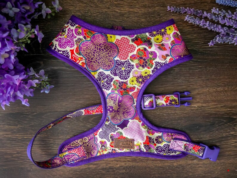May include: Purple dog harness featuring a floral design in shades of pink, red, gold, and white. The harness has a buckle fastening and a D-ring for attaching a lead.
