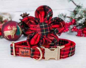 May include: Red and black plaid dog collar with a matching flower accessory. The collar has a gold-colored buckle and a small brown tag with a logo. The flower is in the shape of a large blossom.