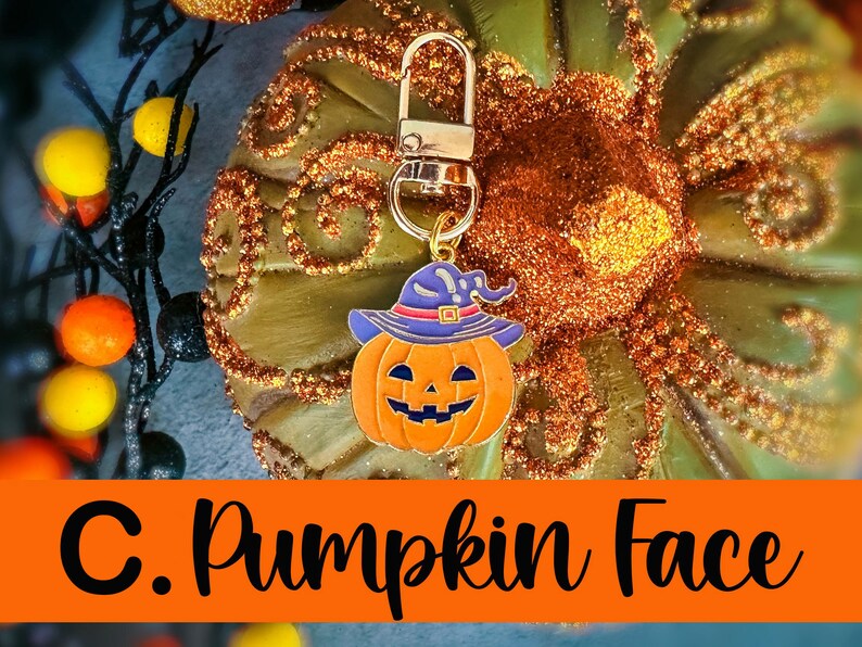 Pode incluir: Um chaveiro com tema de Halloween com um rosto de ab&oacute;bora laranja sorridente usando um chap&eacute;u de bruxa roxo e um fecho dourado. O texto "C. Pumpkin Face" &eacute; exibido em uma faixa laranja abaixo.