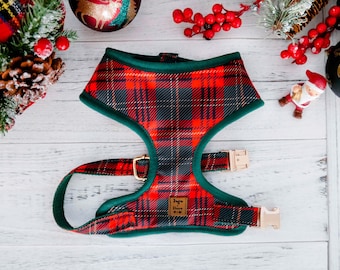 May include: A red, black, and green plaid dog harness with gold-colored buckles and green trim. The harness has a label that reads "Juju House M-M". The harness is designed for a small dog.