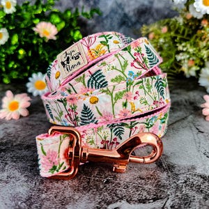 Puede incluir: Un juego de correa y collar para perros con un cierre de oro rosa. La correa y el collar presentan un fondo blanco con un estampado de flores rosas, amarillas y azules y hojas verdes. La marca "Juju Nana" est&aacute; en el collar.