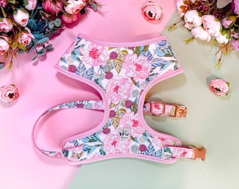 Puede incluir: Un arnés para perro rosa floral con una hebilla dorada. El arnés tiene un fondo blanco con un patrón floral rosa. El arnés está hecho de un material suave y cómodo.