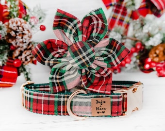 Könnte beinhalten: Ein festliches Hunde-Halsband- und Blumen-Accessoire-Set. Das Halsband und die Blume sind aus rot-grün-weißem Karostoff gefertigt. Das Halsband hat eine goldfarbene Schnalle und ein kleines braunes Etikett mit dem Text "Juju + Nara". Die Blume hat die Form einer sechsblättrigen Blüte.