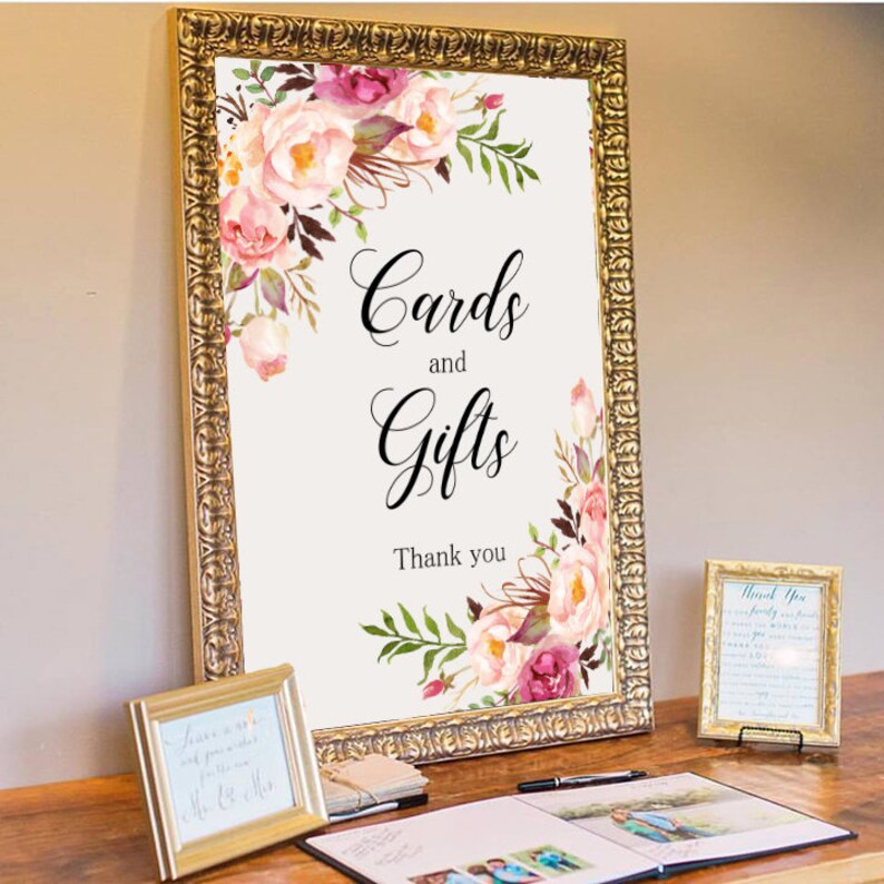 May include: A white sign with a gold frame and floral design. The sign reads "Cards and Gifts" with the text "Thank you" below.