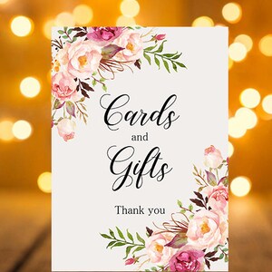 May include: A white card with pink and purple floral designs on the top and bottom. The card says "Cards and Gifts" in black cursive font and "Thank you" in black font.