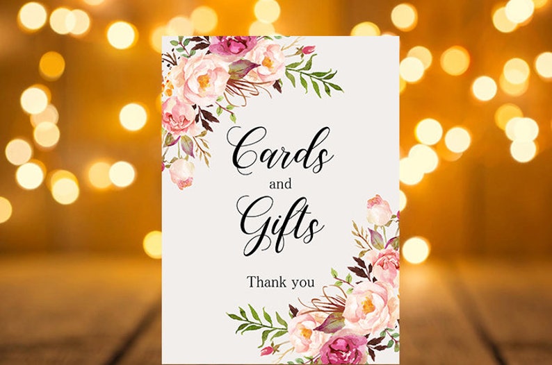 May include: A white card with pink and purple floral designs on the top and bottom. The card says "Cards and Gifts" in black cursive font and "Thank you" in black font.