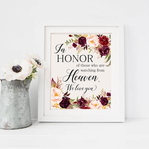 May include: A white framed sign with a floral design in shades of burgundy, pink, and green. The sign reads "In honor of those who are watching from Heaven. We love you."