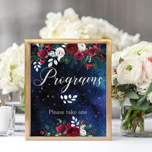 Op de afbeelding: Een ingelijst bord met het woord "Programs" in elegant schrift, omringd door bloemstukken van rode en witte rozen en groen. Het bord bevat ook de tekst "Please take one" in een gouden lijst.