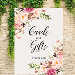 May include: A white sign with pink and purple floral designs around the edges. The sign says "Cards and Gifts" with the text "Thank you" below.