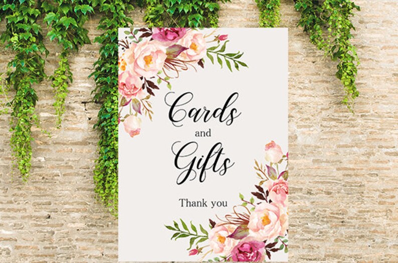 May include: A white sign with pink and purple floral designs around the edges. The sign says "Cards and Gifts" with the text "Thank you" below.