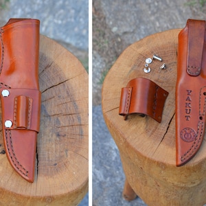 May include: A brown leather knife sheath with a belt loop and a small pouch. The sheath is stitched with black thread and has the word "YAKUT" stamped on it. The sheath is shown with its components.