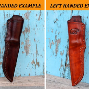May include: Two leather knife sheaths. The sheath on the left is dark brown, and the one on the right is reddish-brown with a bear embossed on the front. Both sheaths have stitched edges and are designed to hold a knife.
