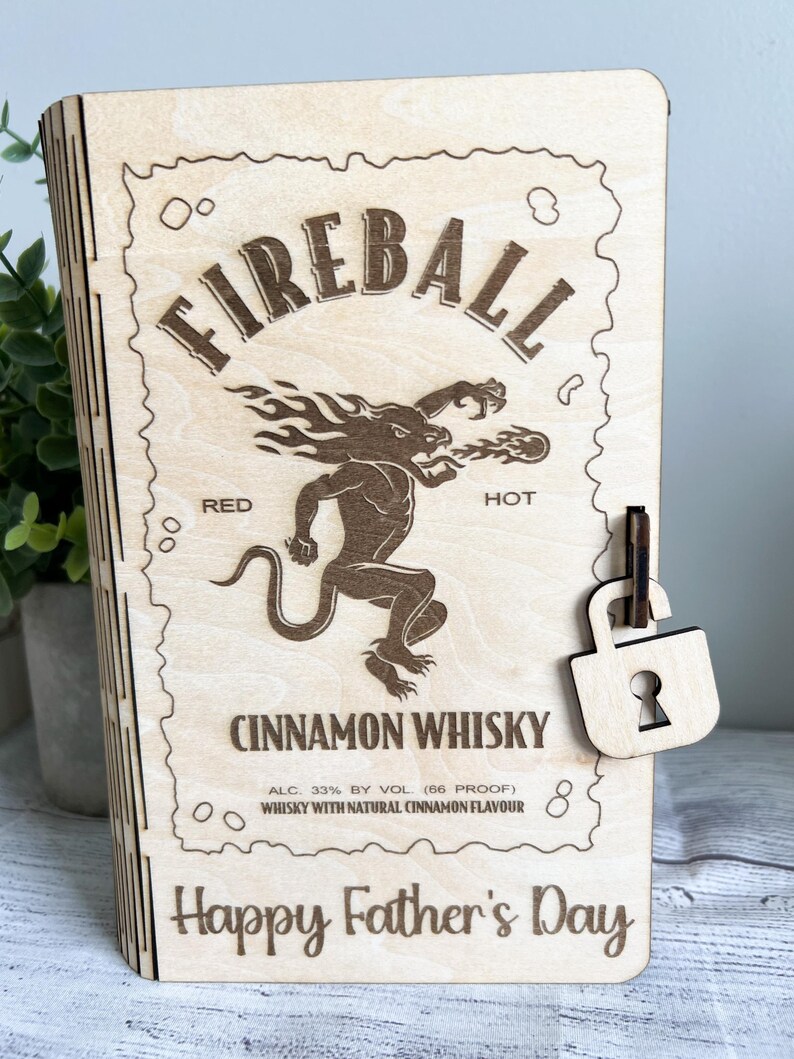 May include: Wooden box with a laser-etched design featuring the Fireball Cinnamon Whisky logo, a mythical creature, and the text "Happy Father's Day." Includes a wooden padlock closure.