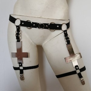 Op de afbeelding: Zwart lichaamsharnas met zilverkleurige metalen accenten en grote omgekeerde kruisbedels. Het harnas bevat een tailleband, beenbanden en verbindingsketens. Getoond op een mannequin.